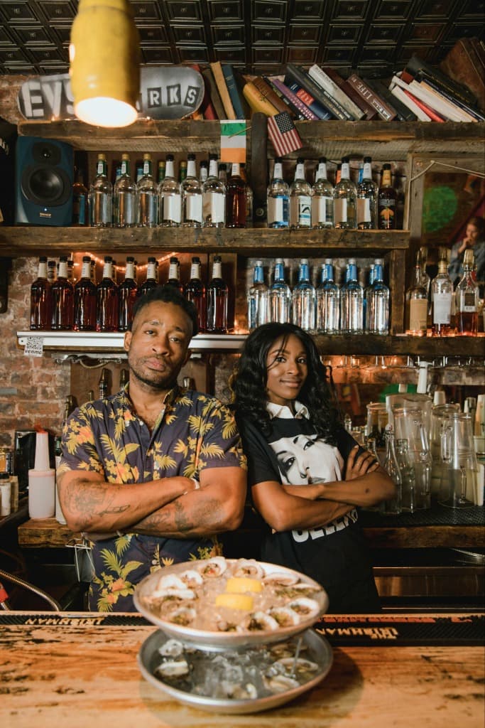 Two bar owners smiling behind their bar